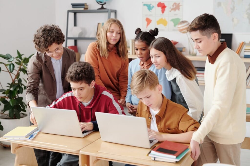 pexels photo 5212687 A group of diverse students collaborating on laptops in a classroom setting, guided by a teacher.